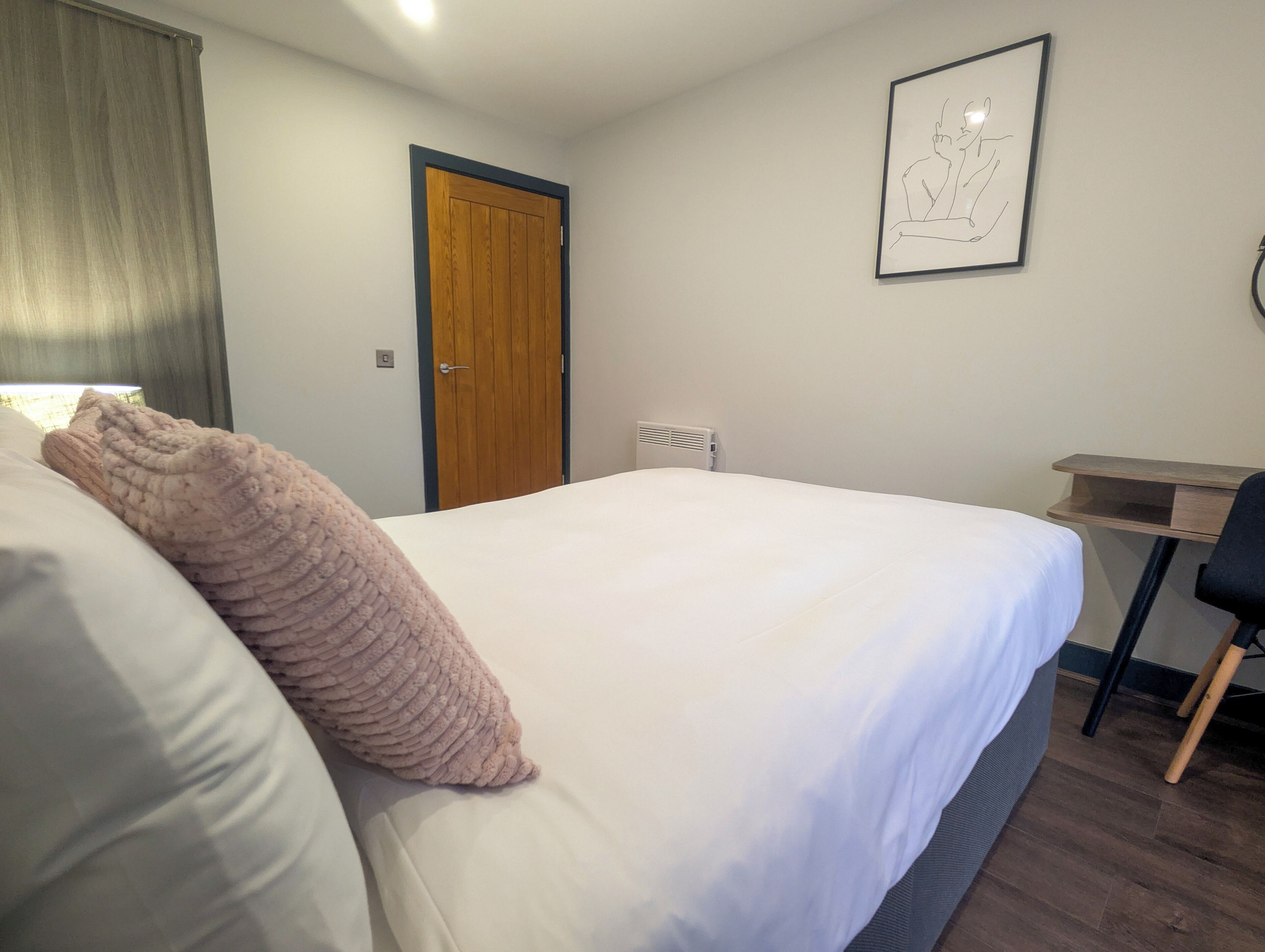 Een slaapkamer met een groot bed, een houten deur, een bureau en een lijst met kunstwerk aan de muur.