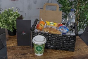 A wicker basket filled with snacks, a water bottle, and a coffee cup on a wooden table.