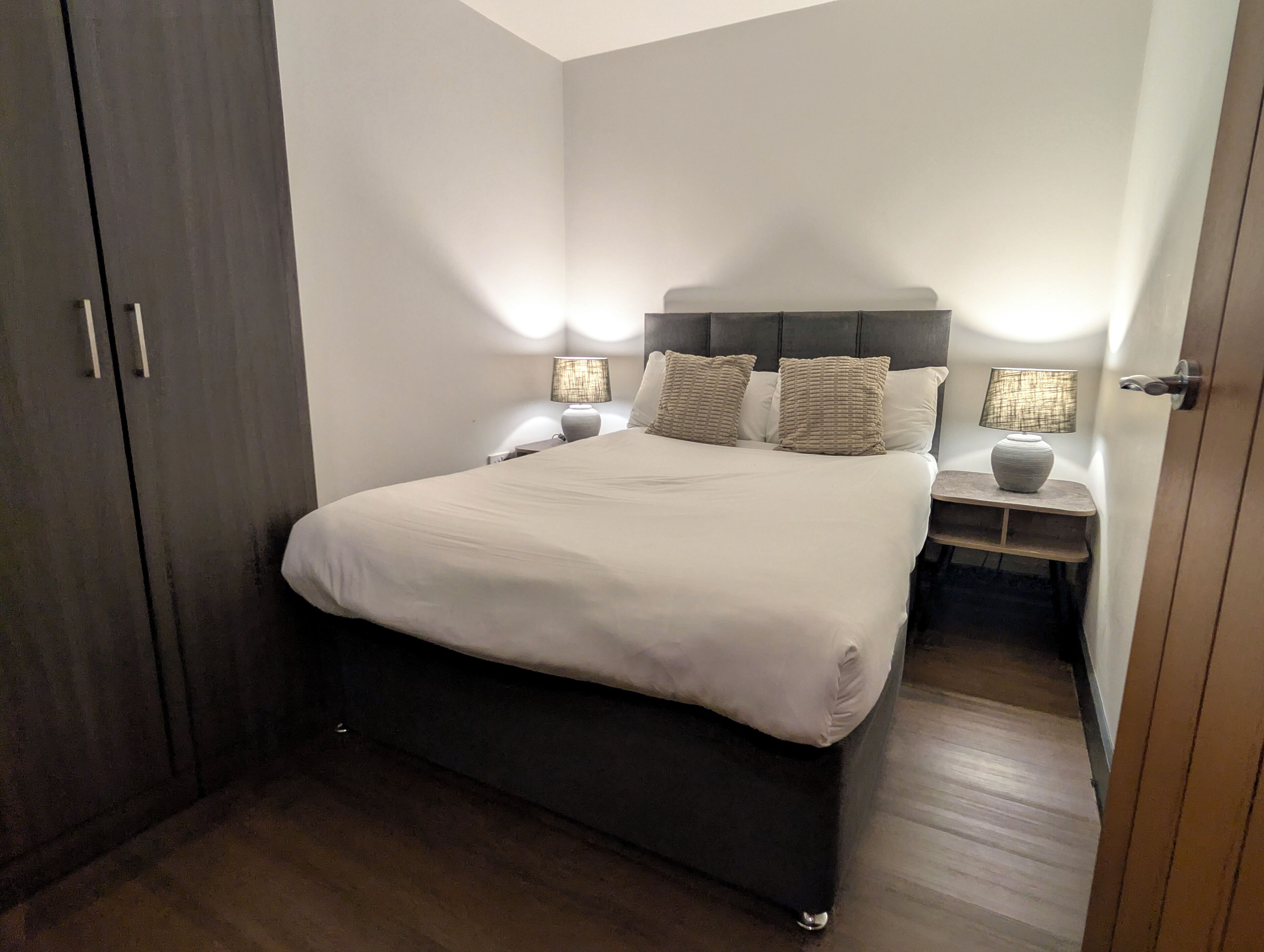A bedroom with a bed, bedside tables, lamps, and a wardrobe.
