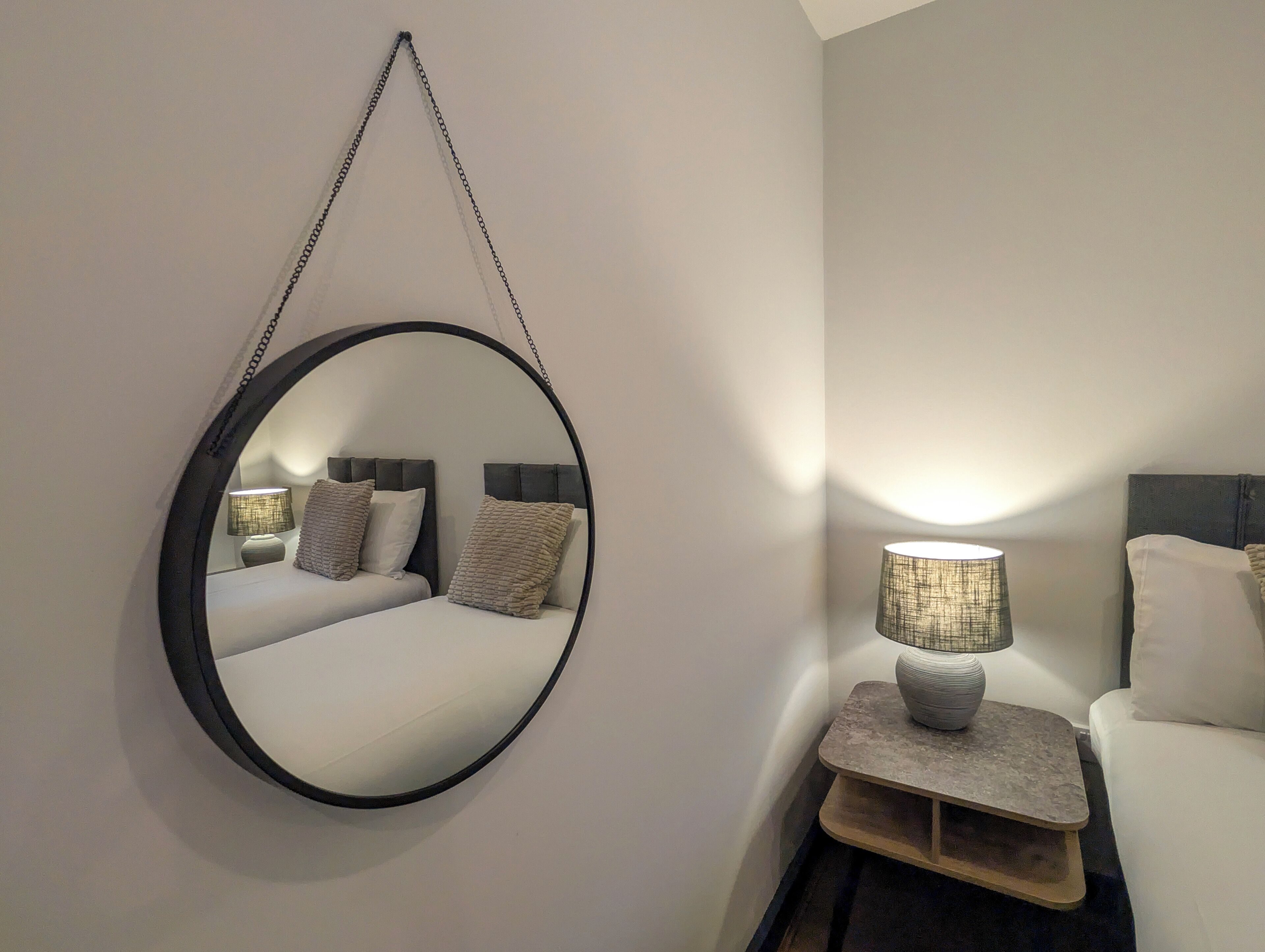 Una camera da letto con uno specchio rotondo, una lampada da comodino e un letto con due cuscini.