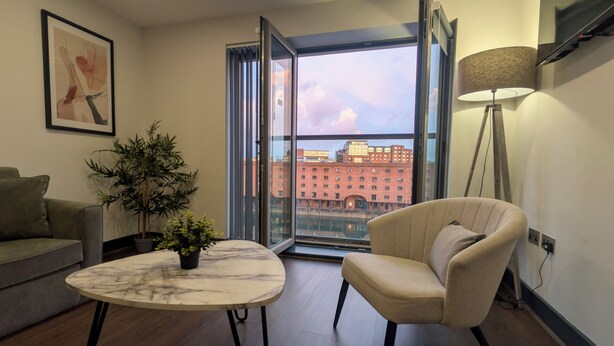 Ein modernes Wohnzimmer mit einem Marmortisch, einer Couch, einem Sessel, einer Topfpflanze und Blick auf eine Stadtlandschaft durch ein großes Fenster.