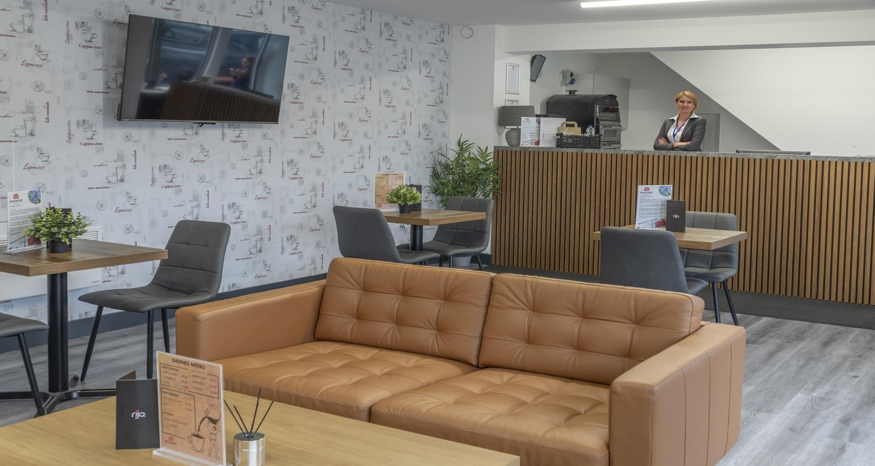 A modern office space with a leather sofa, wooden tables, and a reception area with a coffee machine.