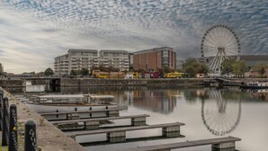 Ein Ufergebiet mit einem Riesenrad, Booten, die an der Küste liegen, und Gebäuden im Hintergrund.