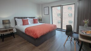 Ein modernes Hotelzimmer mit einem großen Bett, einem Schreibtisch und einem Stuhl. Ein Fenster bietet Blick auf ein Backsteingebäude.
