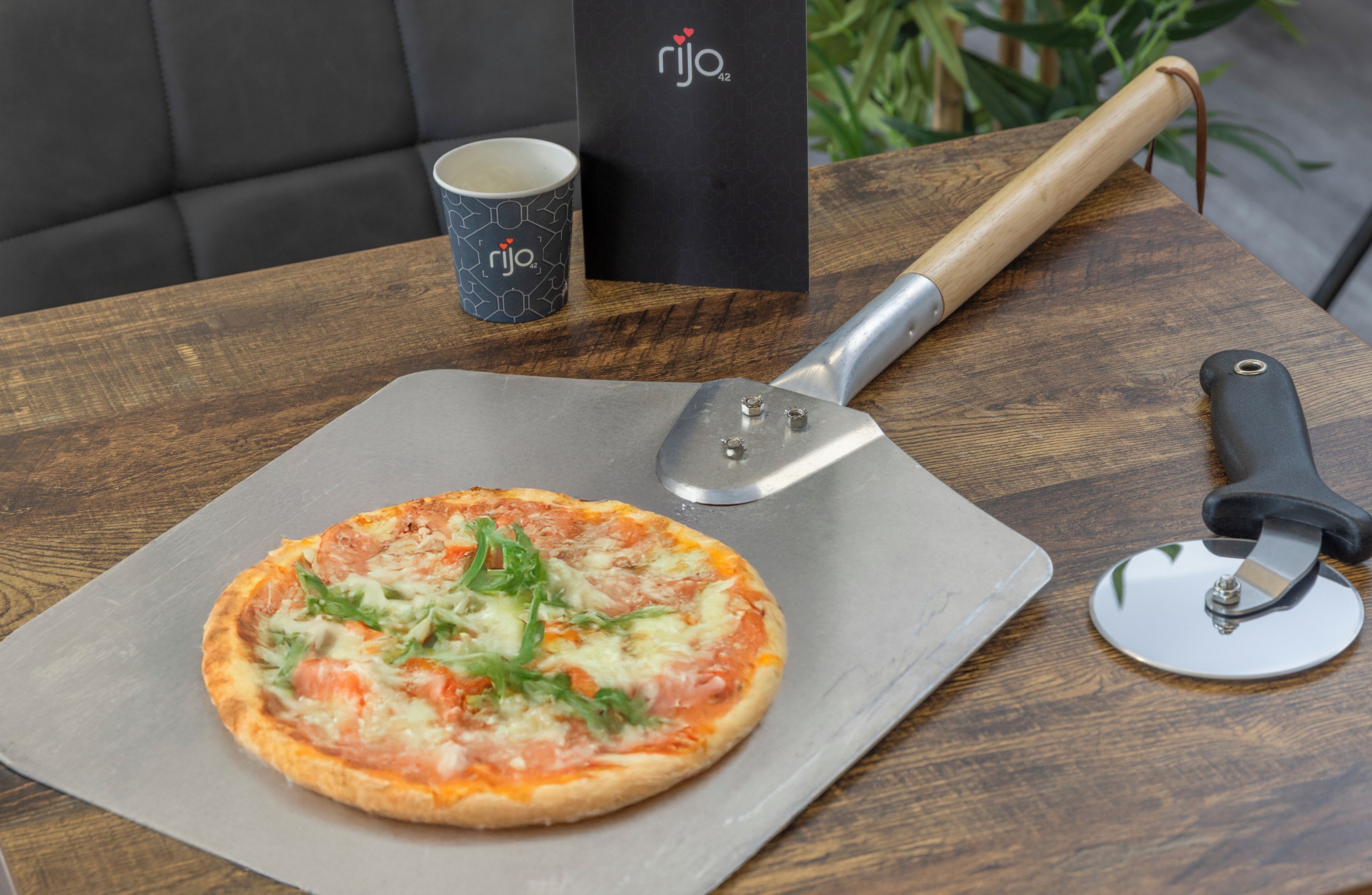 Pizza sobre una taula de fusta, amb un tallapizzes i una tassa amb el logotip de la marca.