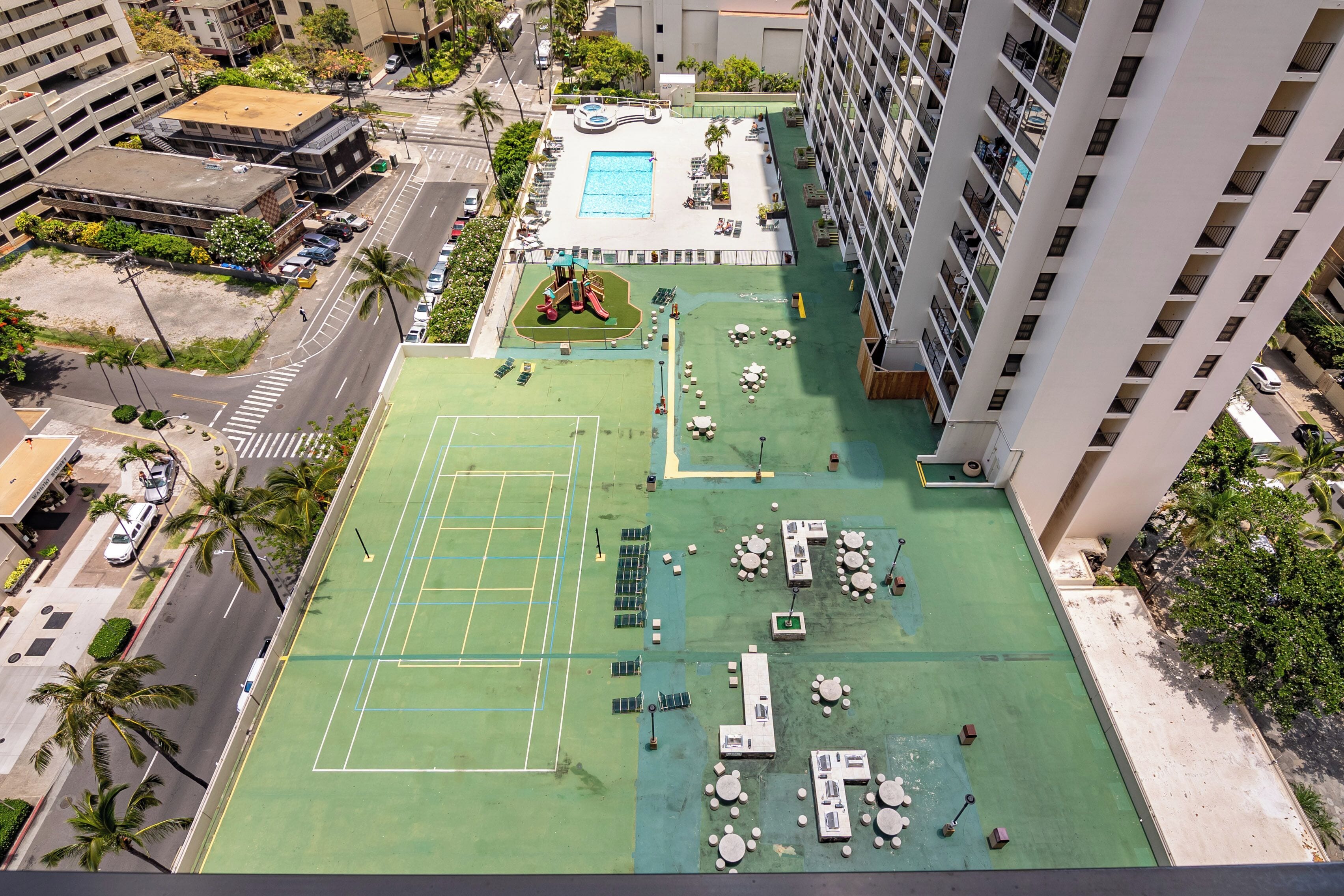 An aerial view of a rooftop with a tennis court, pool, and lounge area.