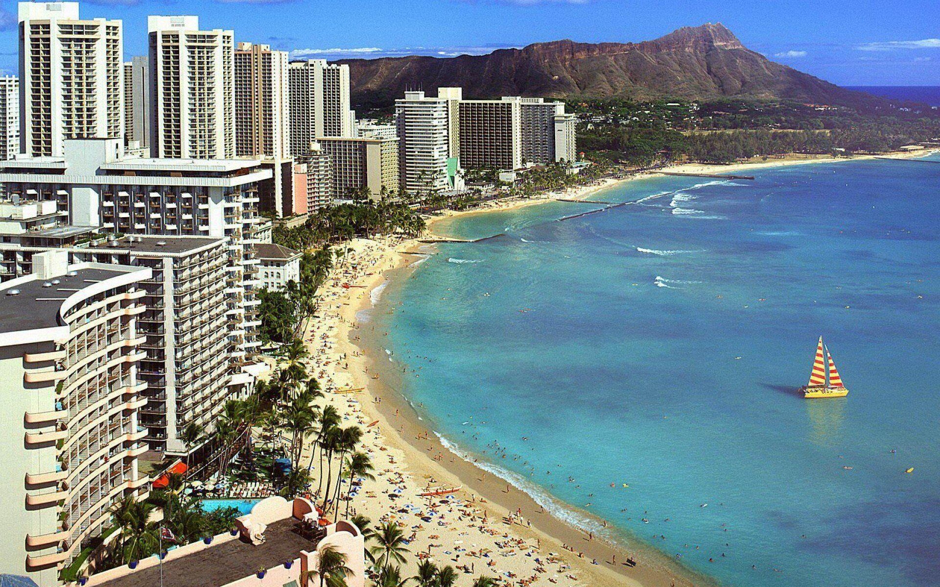A coastal cityscape with high-rise buildings, a beach, and a mountain in the background.