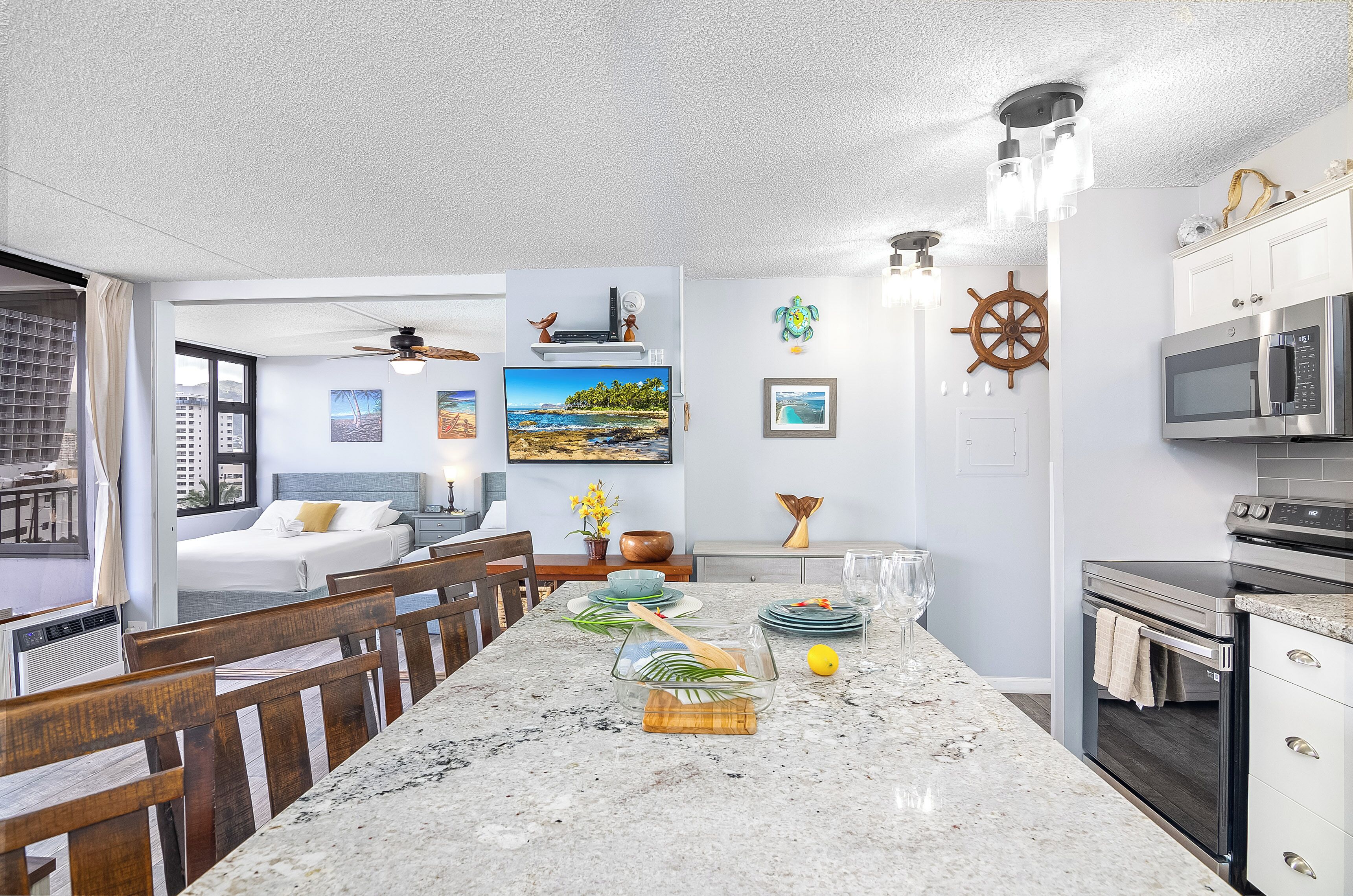 Una cocina moderna con una isla grande, horno empotrado y microondas. Hay una zona de comedor con sillas de madera y una mesa. La habitación tiene vistas al horizonte de la ciudad.