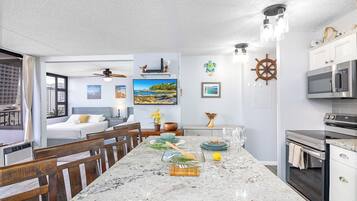 Una cocina moderna con una isla grande, horno empotrado y microondas. Hay una zona de comedor con sillas de madera y una mesa. La habitación tiene vistas al horizonte de la ciudad.