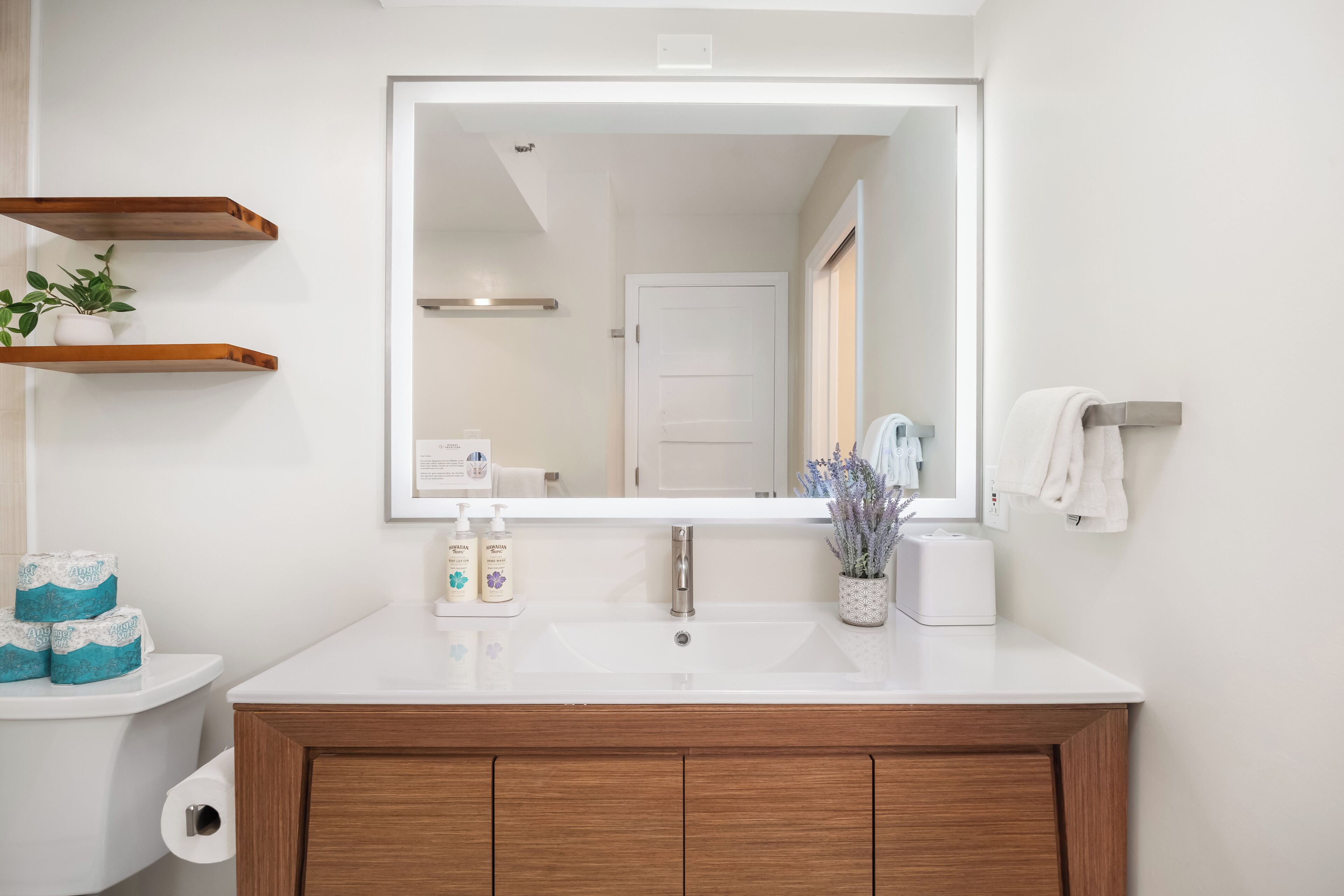 Ein Badezimmer mit weißem Waschbecken, Holz-Waschmöbel, einem großen Spiegel und einer Toilette mit Toilettenpapier.
