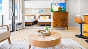 Et hotelværelse med to senge, et spisebord og et stort vindue.