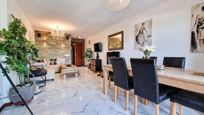A modern living room with a dining area, featuring a marble floor, a chandelier, a sofa, a coffee table, and a TV. - Cozy Seaside Apartment in Manilva (Manilva)