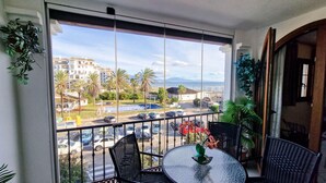 A balcony with a view of a parking lot, palm trees, and buildings. - Cozy Seaside Apartment in Manilva (Manilva)