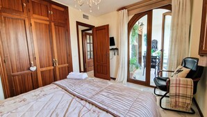 A bedroom with a large bed, wooden wardrobe, and a chair with a blanket. - Cozy Seaside Apartment in Manilva (Manilva)