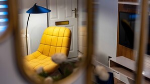 Ein gelber Sessel mit Kissen, eine blaue Stehlampe und ein Fernseher auf einem Holzständer.