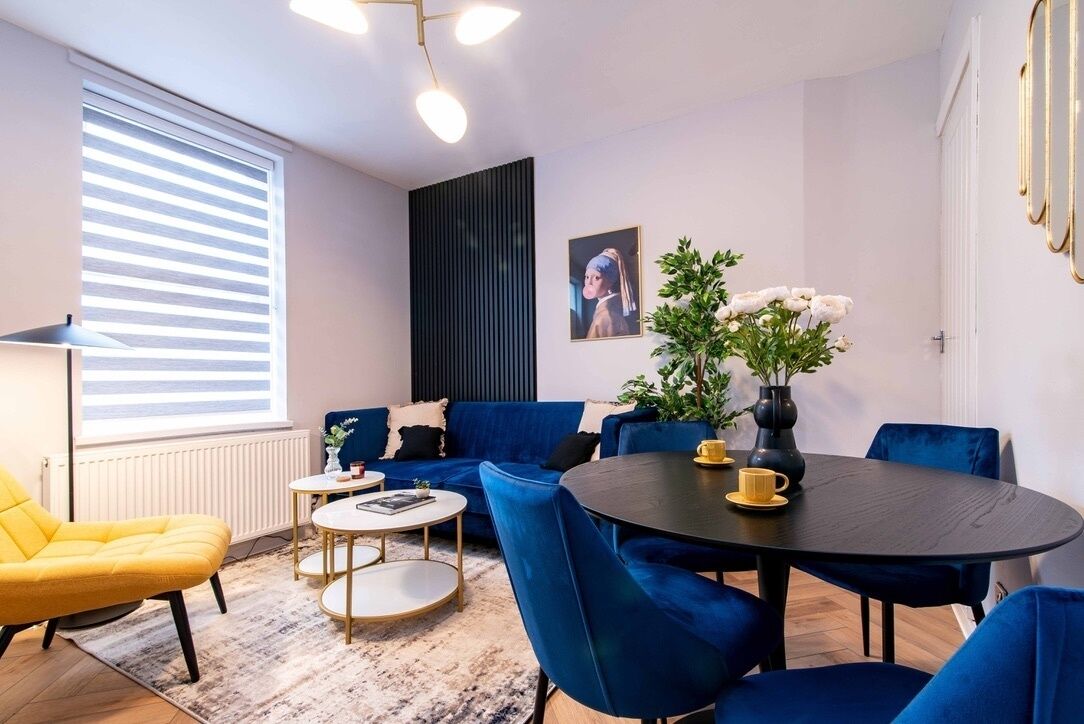 Una sala moderna con un sofá azul, un sillón amarillo y una mesa de comedor redonda.