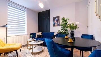 Una sala moderna con un sofá azul, un sillón amarillo y una mesa de comedor redonda.