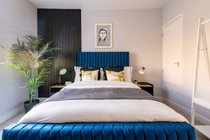 A modern bedroom with a large bed, a blue upholstered headboard, a potted plant, a framed artwork on the wall, and a white door. - Stylish, sleeps 3, Sheffield city centre, parking (Sheffield)