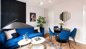 Ein modernes Wohnzimmer mit einem blauen Sofa, einem runden Couchtisch und einem Essbereich mit blauen Stühlen und einem schwarzen Tisch.