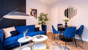 Ein modernes Wohnzimmer mit einem blauen Sofa, einem Esstisch mit blauen Stühlen, einer Stehlampe und einer Pflanze.
