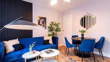 Una sala de estar moderna con un sofá azul, una mesa de comedor con sillas azules, una lámpara de pie y una planta.