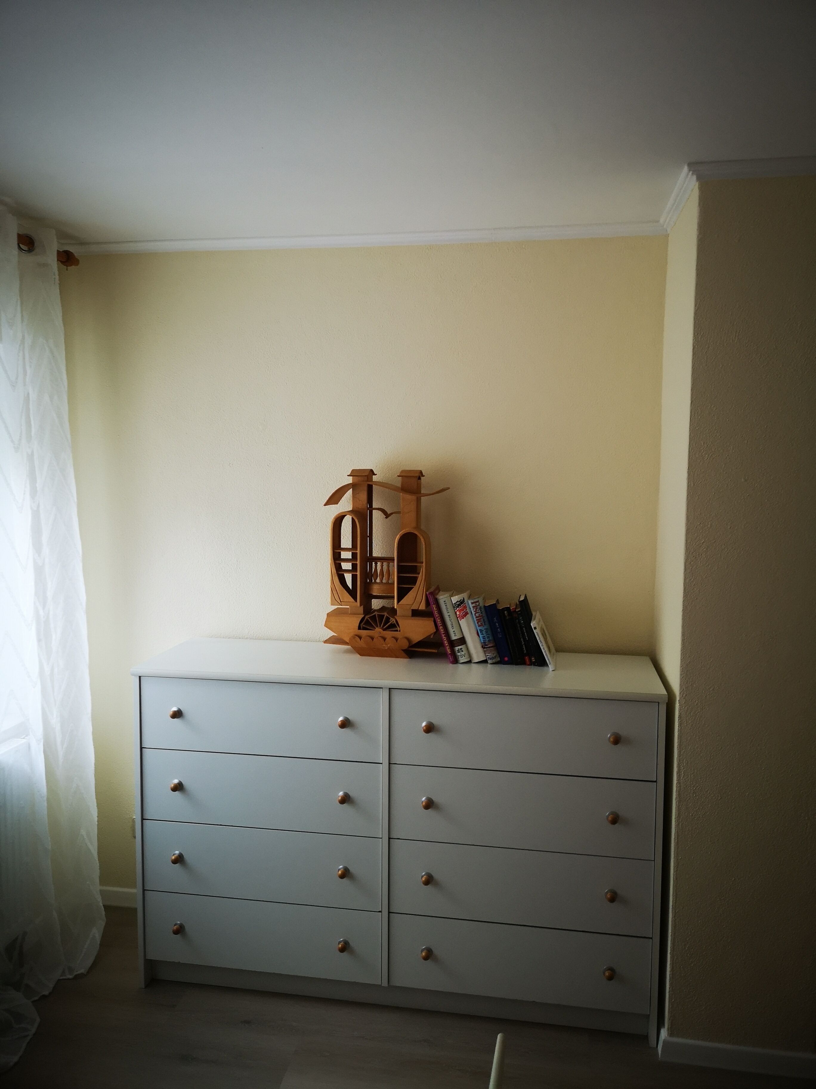 Una habitación con un aparador blanco, un juguete de madera encima y libros a su lado.