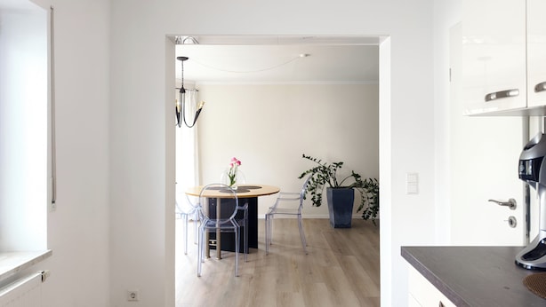 A modern kitchen with a dining area, featuring a round table with chairs, a potted plant, and a water dispenser.