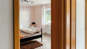 A bedroom with a bed, a window with curtains, a radiator, and a wooden floor.