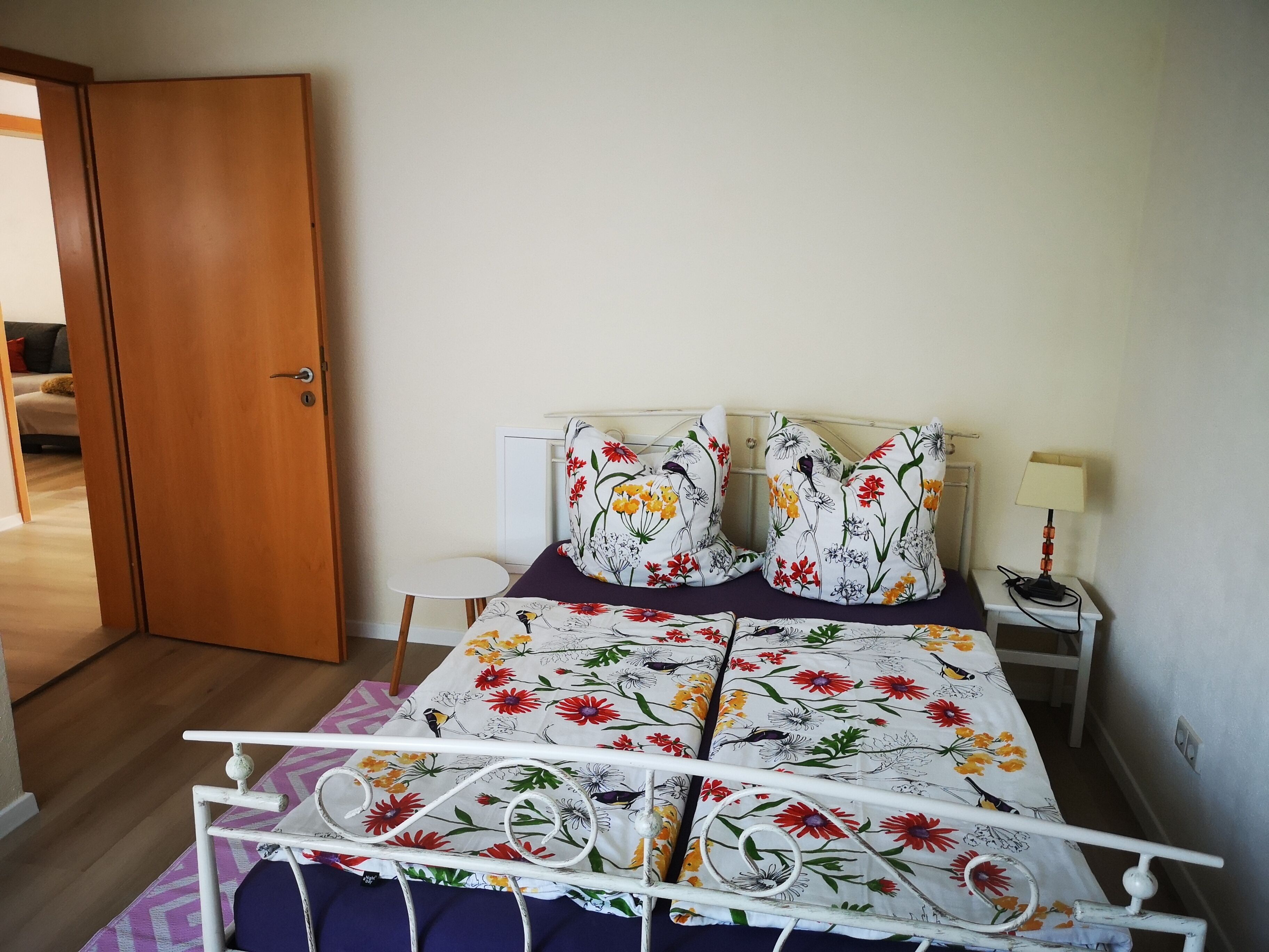 Een slaapkamer met een bed, kussens, een nachtkastje, een lamp en een deur.