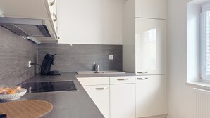 A modern kitchen with a dark countertop, white cabinets, a built-in oven, and a window with blinds.