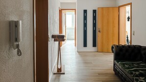 A hallway with a wooden door, a coat rack, and a black leather sofa.