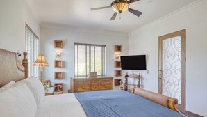 A bedroom with a bed, dresser, television, and decorative wall sconces.