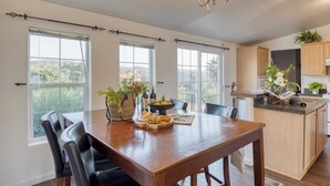 A spacious kitchen with large windows, a dining area with a wooden table and chairs, and a kitchen island with a sink and countertop.