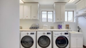 A laundry room with three washing machines, a drying rack, and a sink.