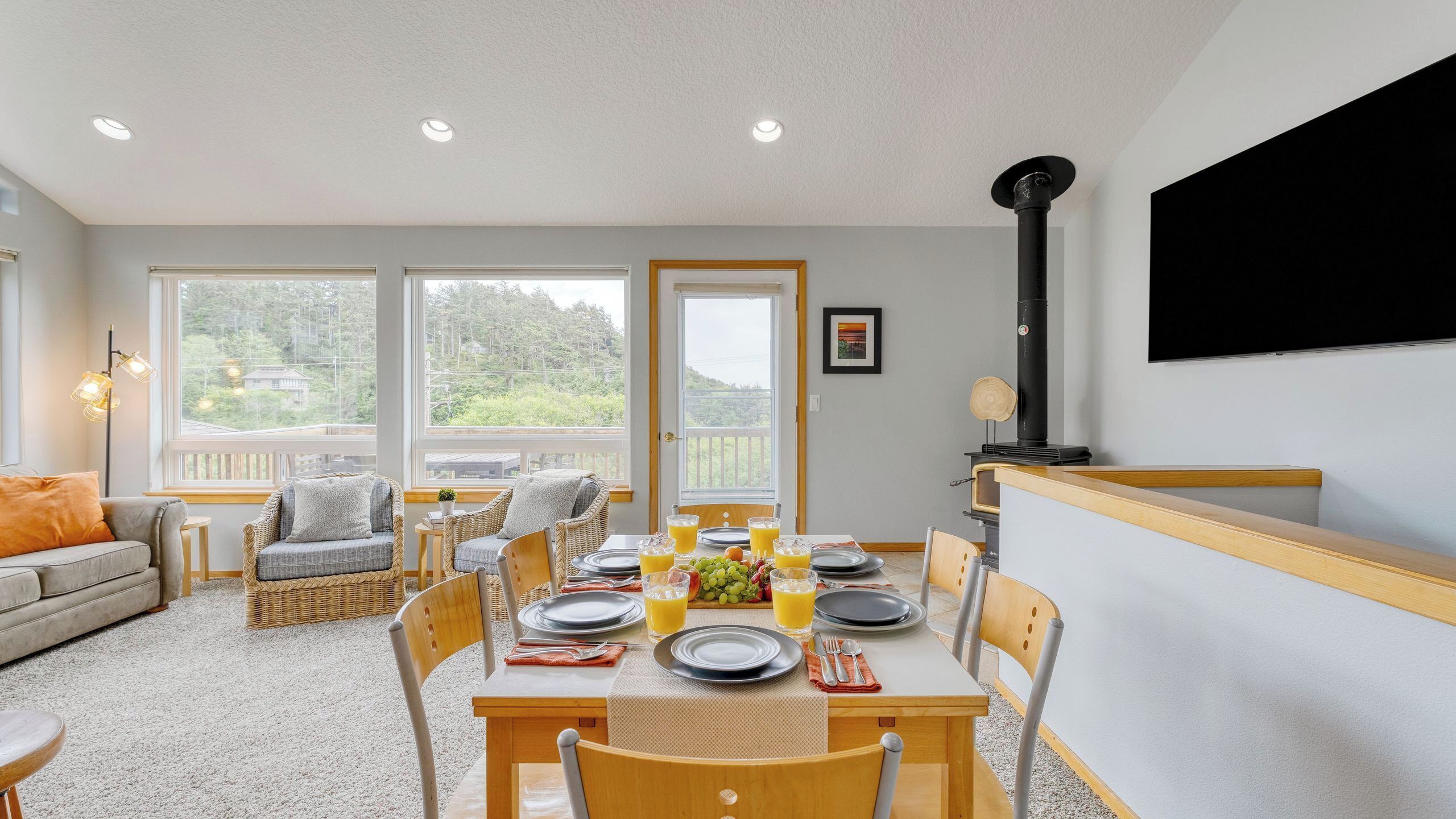 A dining area with a table set for four, a sofa, wicker chairs, and a black stove.