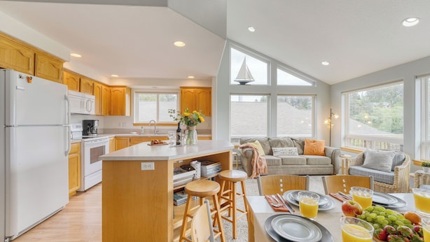 Una cocina moderna con armarios de madera, una isla central y un comedor con una mesa preparada para el desayuno.