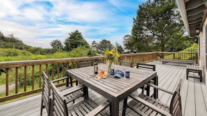 Una terraza de madera con una mesa lista para comer, rodeada de sillas, con vistas a un paisaje exuberante.