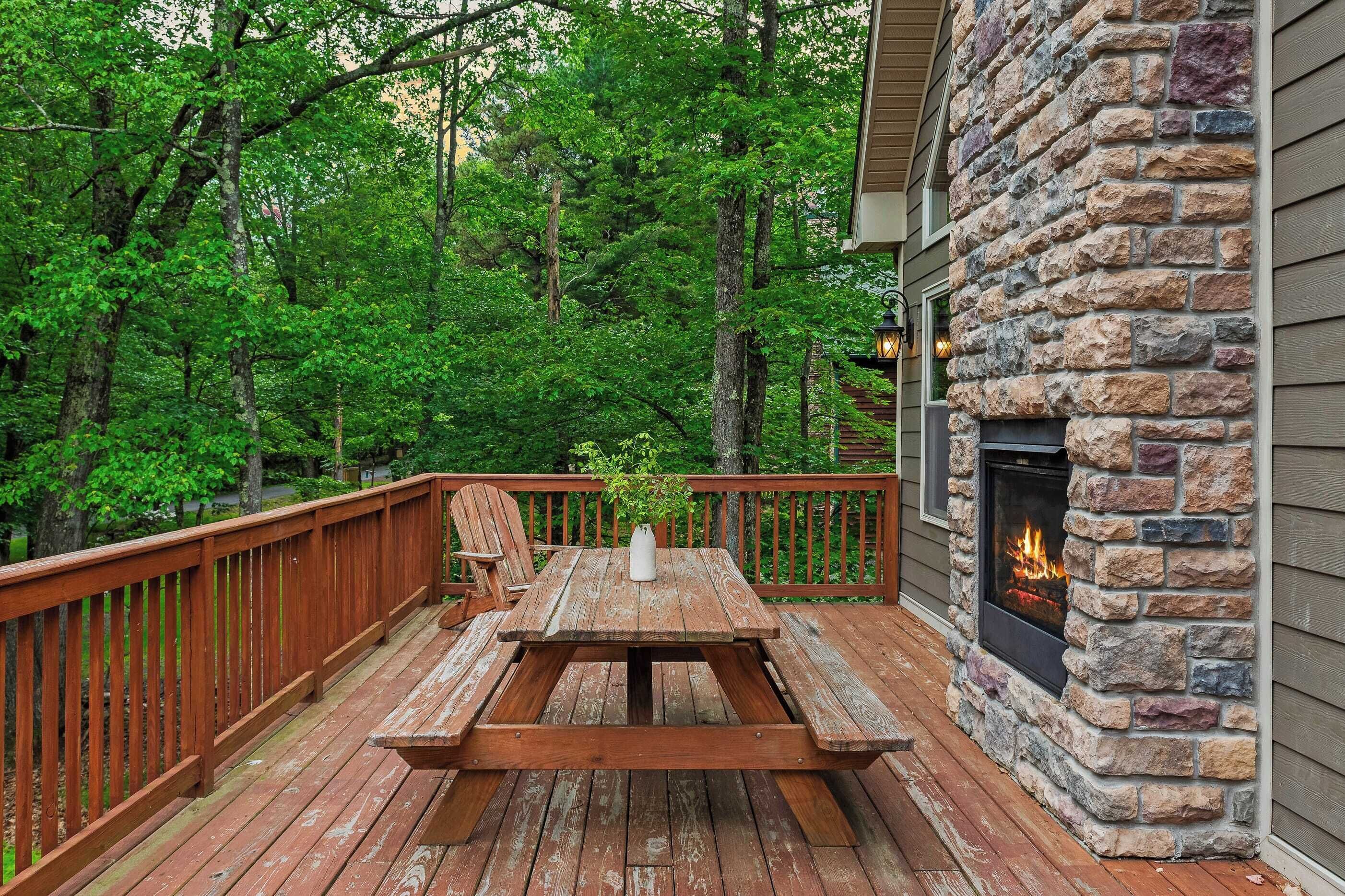 A wooden deck with a stone fireplace, a picnic table, and a chair.