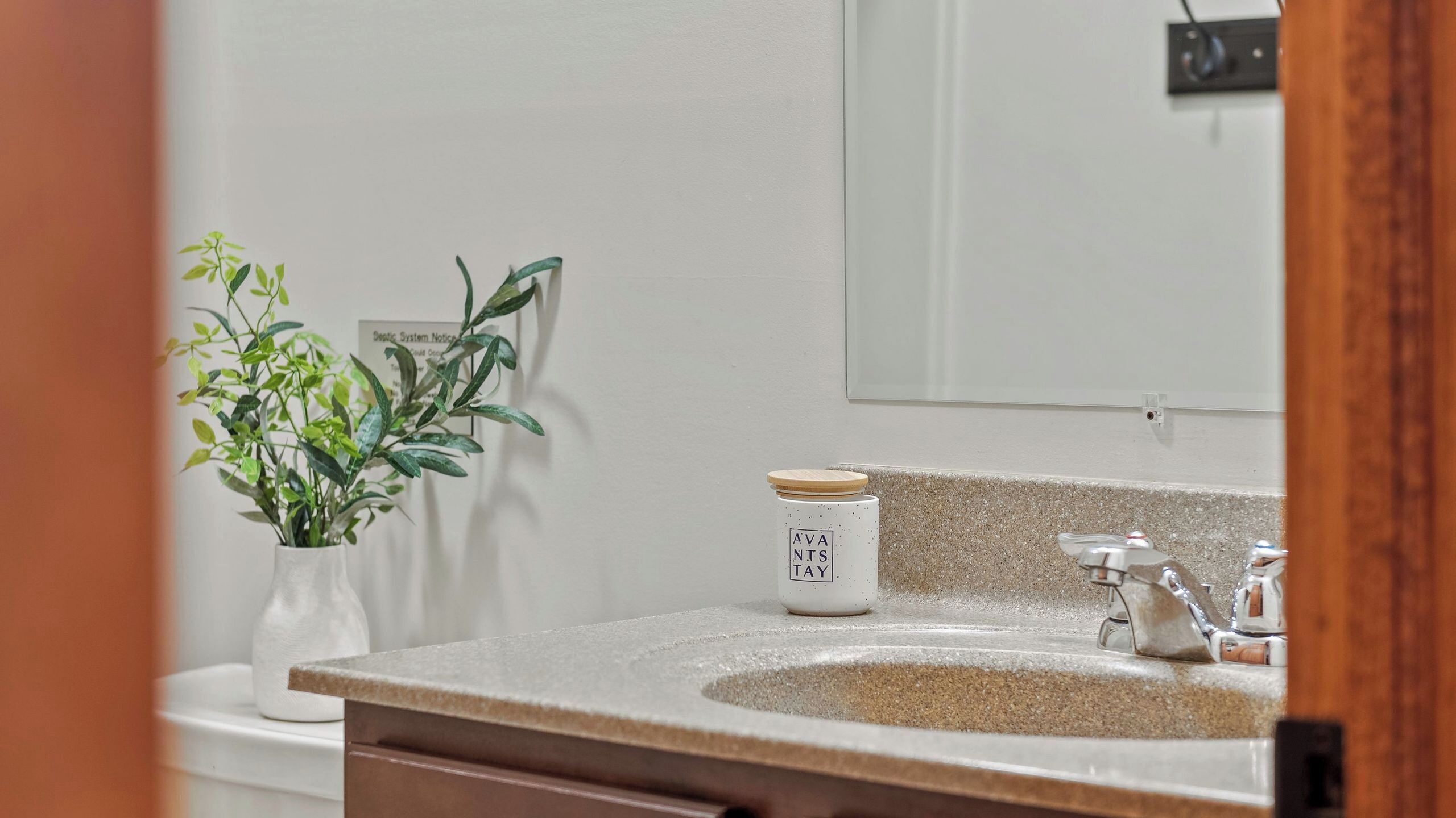 Un baño con un lavamanos blanco, una planta y un cartel en la pared.