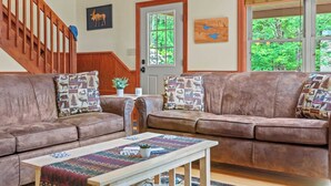 A cozy living room with two brown leather sofas, a wooden coffee table, and a staircase.