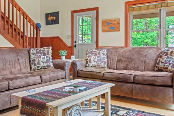 A cozy living room with two brown leather sofas, a wooden coffee table, and a staircase.
