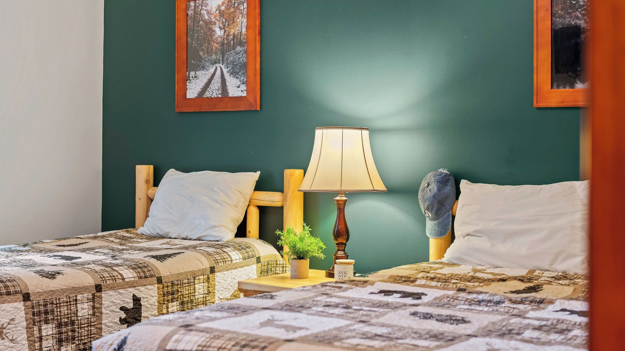 A bedroom with two beds, a nightstand with a lamp, a small plant, and a framed picture on the wall.
