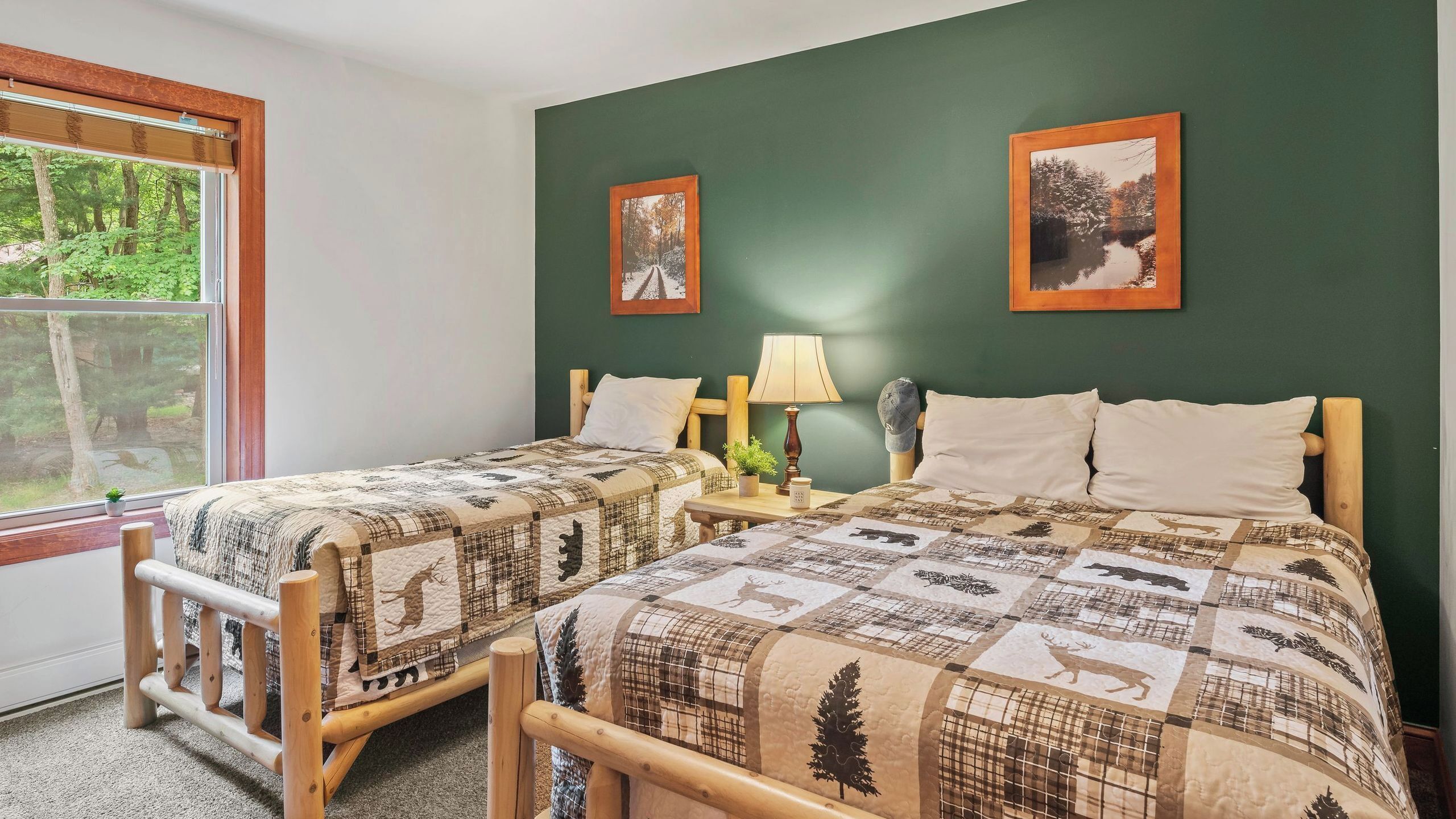 A room with two beds, a window with a view of trees, and two framed pictures on the wall.