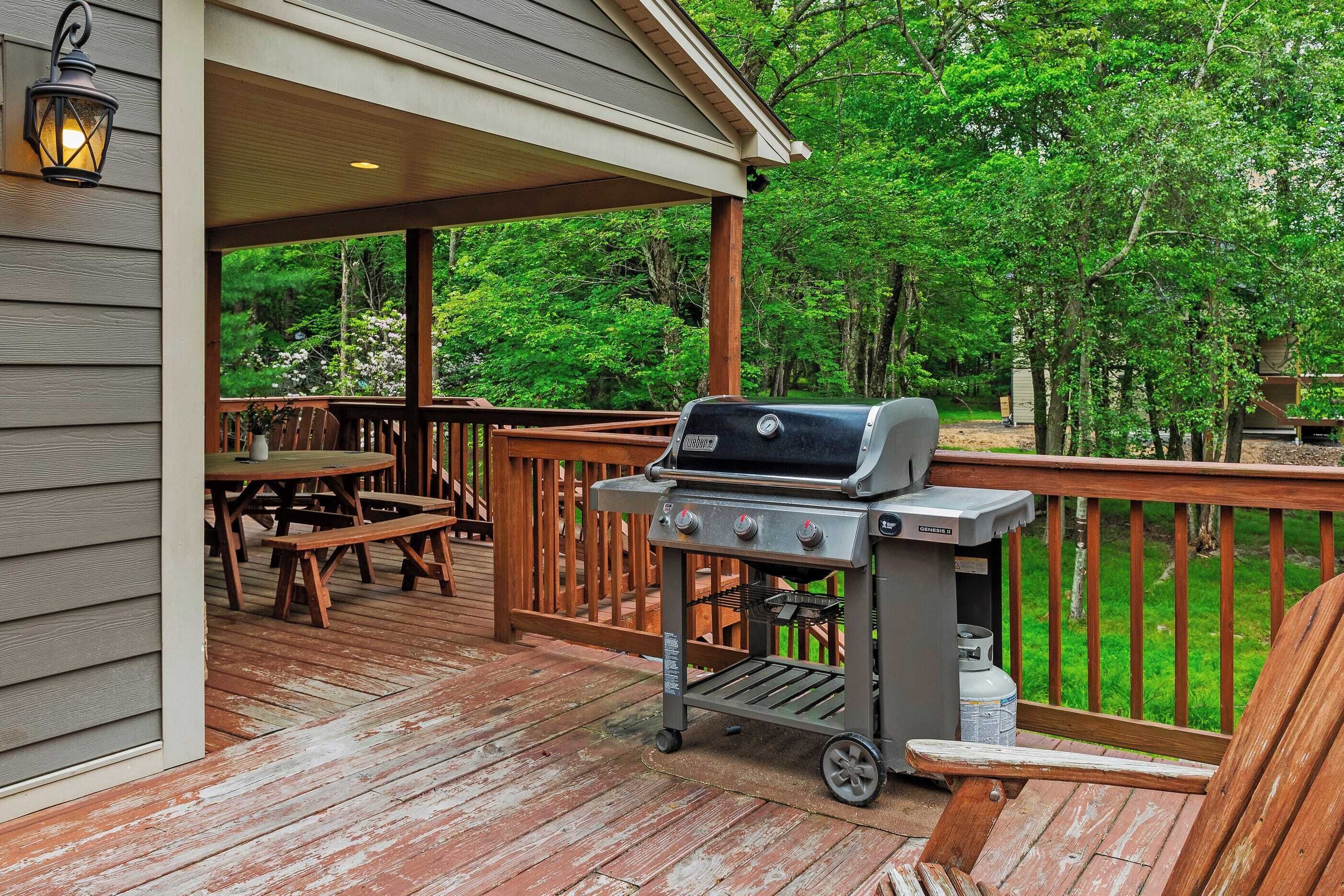 A wooden deck with a grill, picnic table, and outdoor seating area.