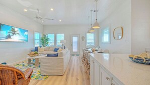 Eine geräumige Küche mit großer Kochinsel, weißen Schränken und einem Essbereich mit Korbstühlen.