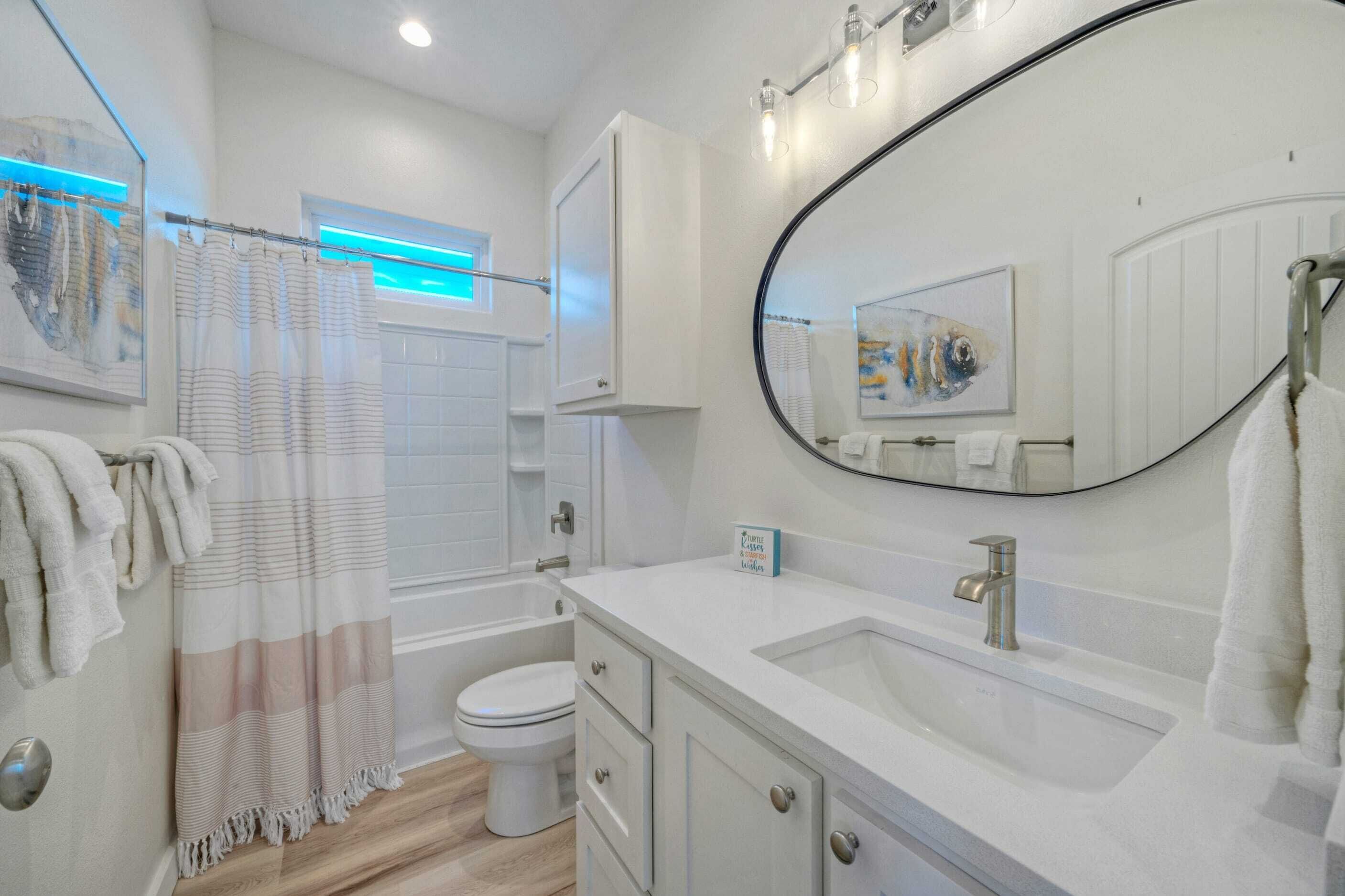 A modern bathroom with a bathtub, toilet, and sink. There is a large mirror above the sink and a shower curtain with a striped pattern.