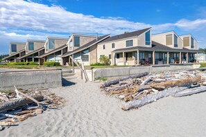 Eine Reihe moderner Strandhäuser mit großen Fenstern, ein Sandstrand davor und ein klarer, blauer Himmel.