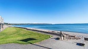 A coastal view with a grassy area, a paved walkway, and a wooden structure by the water. - Beachcomber's Bliss by Avantstay Steps to the Beach Ocean Views (Freeland)
