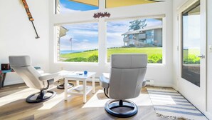 Een moderne kamer met een groot raam, een witte stoel, een klein tafeltje en uitzicht op een huis en groen.