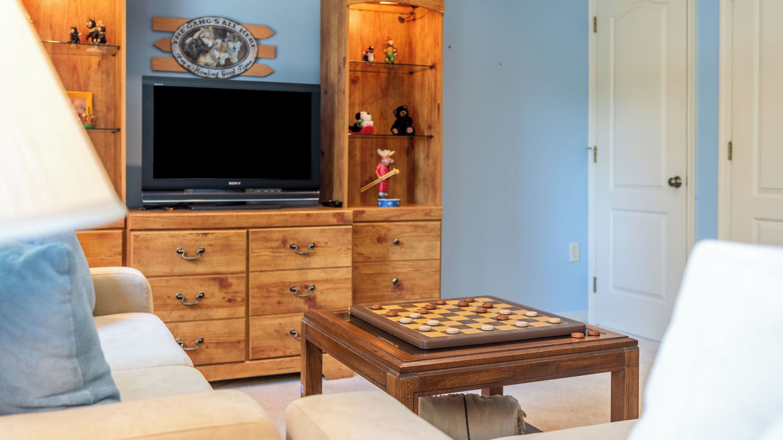 A living room with a television, wooden cabinets, a chess table, and a door.